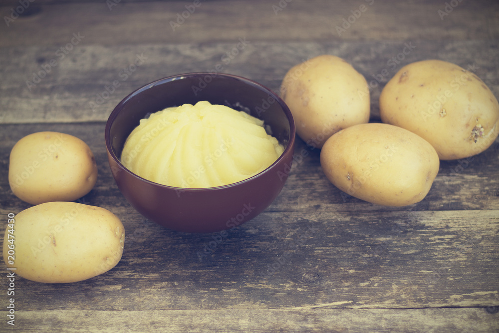 Mashed potatoes and raw potatoes side by side, located on a wooden background, rustic style close-up