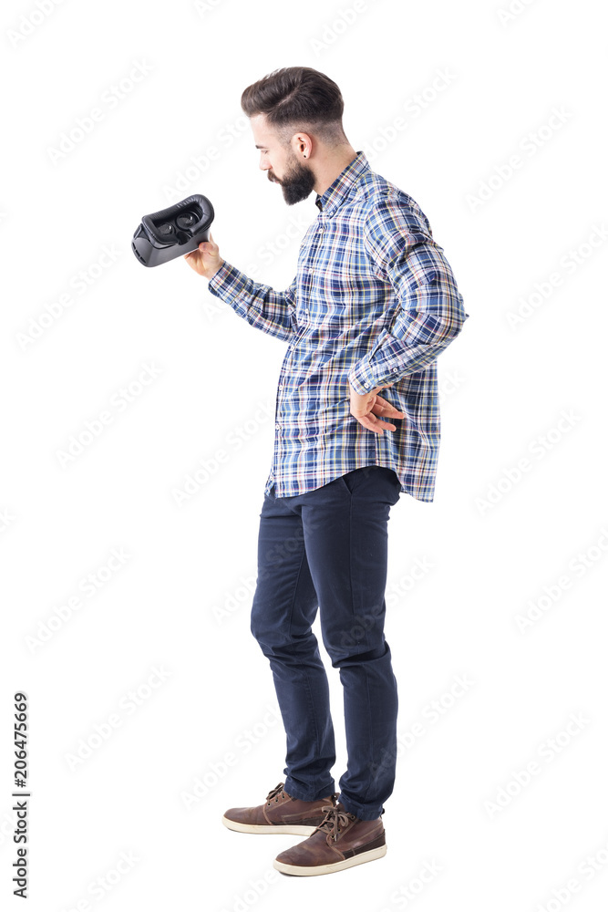 Young suspicious bearded man examining or inspecting virtual reality headset. Full body isolated on white background. Young suspicious bearded man examining or inspecting virtual reality headset. Full body isolated on white background.