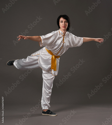 Young woman practicing tai chi chuan. Chinese management skill Qi's energy. Gray background, studio shoot.