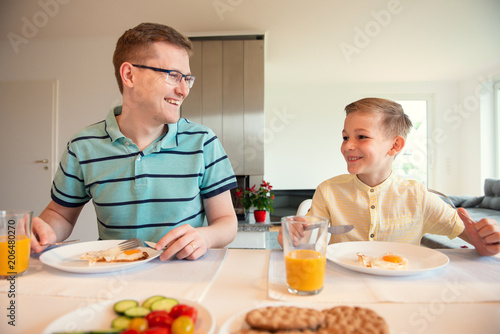 Happy young father with his cute son talking at the breakfast