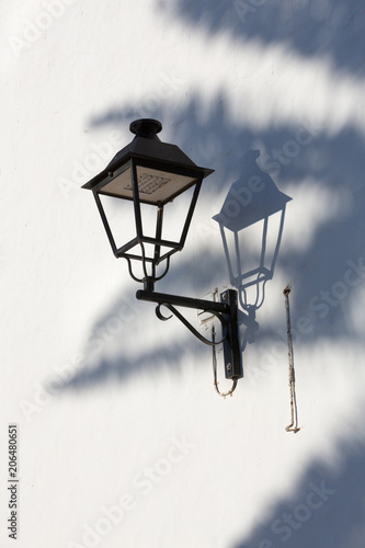 Streetlantern on a white wall with shadows of a palm leaf. photo