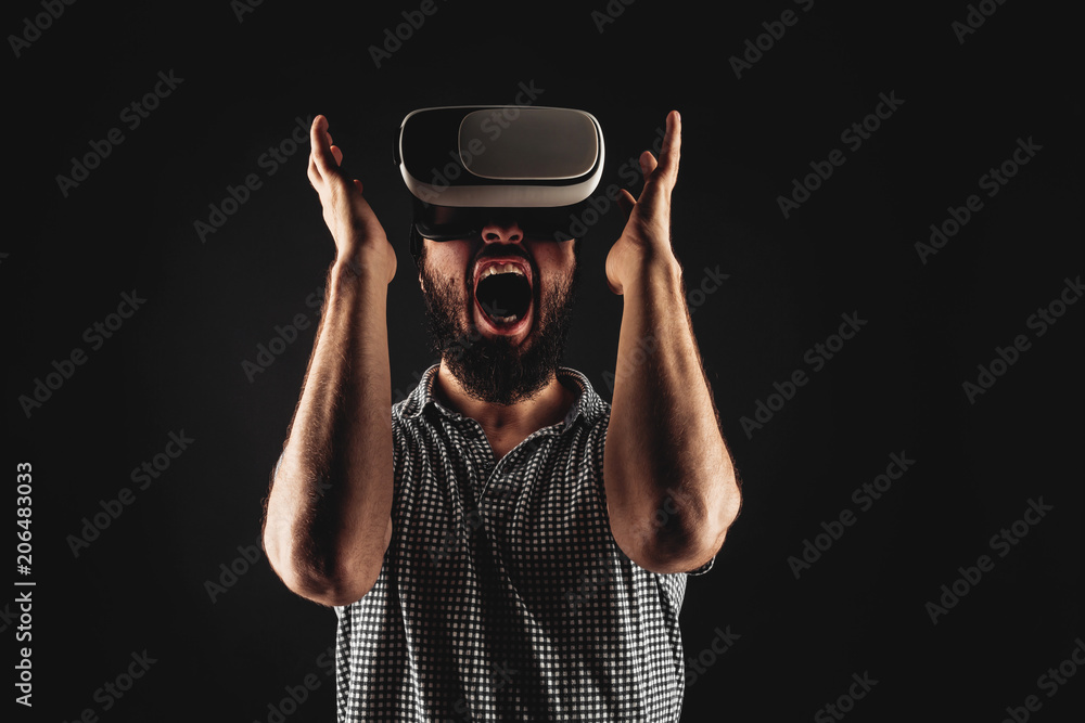 A bearded man in a helmet of virtual reality get fear. Studio shot. Black background A bearded man in a helmet of virtual reality get fear. Studio shot. Black background