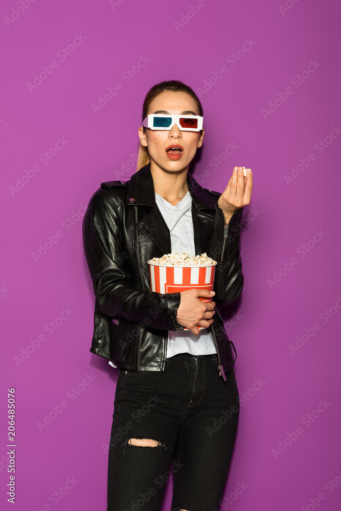 shocked asian girl in leather jacket and 3d glasses eating popcorn and looking at camera isolated on violet shocked asian girl in leather jacket and 3d glasses eating popcorn and looking at camera isolated on violet