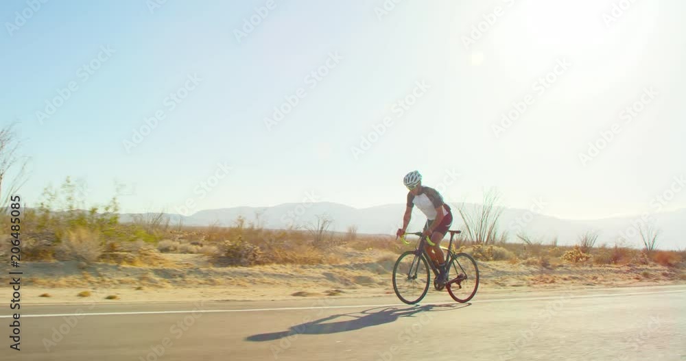 Slow motion young man cycling on road bike outside on desert road on sunny day Slow motion young man cycling on road bike outside on desert road on sunny day