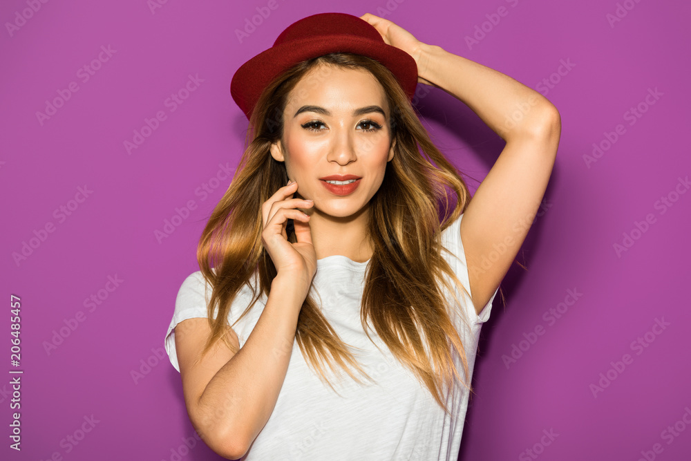 portrait of beautiful stylish asian girl in hat smiling at camera isolated on violet portrait of beautiful stylish asian girl in hat smiling at camera isolated on violet