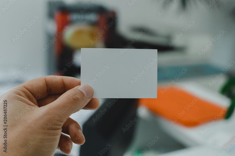 Closeup image of holding business card, person hand showing plain mock up space on professional office background. Businessman communication information Closeup image of holding business card, person hand showing plain mock up space on professional office background. Businessman communication information
