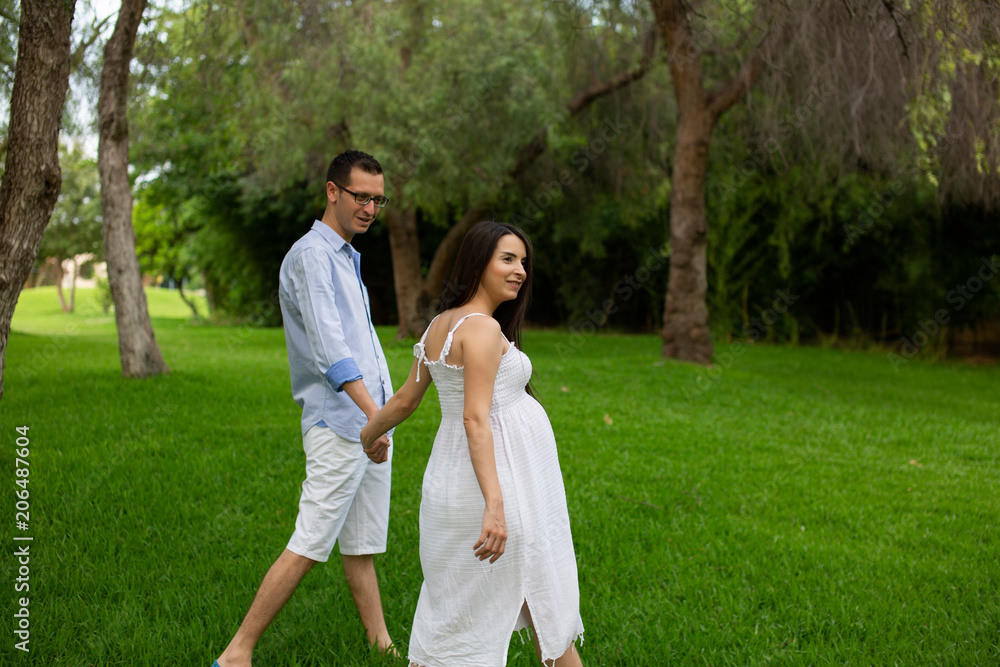 Pregnant couple walks in the park together holding hands Pregnant couple walks in the park together holding hands