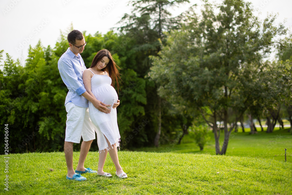 Pregnant couple walks in the park together holding hands Pregnant couple walks in the park together holding hands