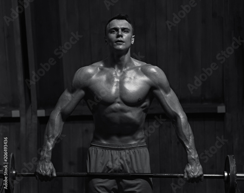 Portrait of young muscular man lifting weights in the gym, black and white image