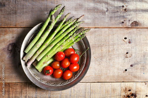 Banches of fresh green asparagus and tomatoes in a metall plate on wooden background