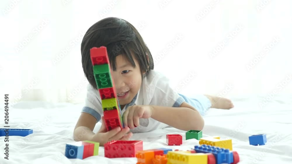 Little asian child playing with colorful construction blocks on white bed Little asian child playing with colorful construction blocks on white bed