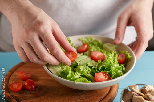 Male hands put cherry tomatoes in the bowl with lettuce salad leaves.
