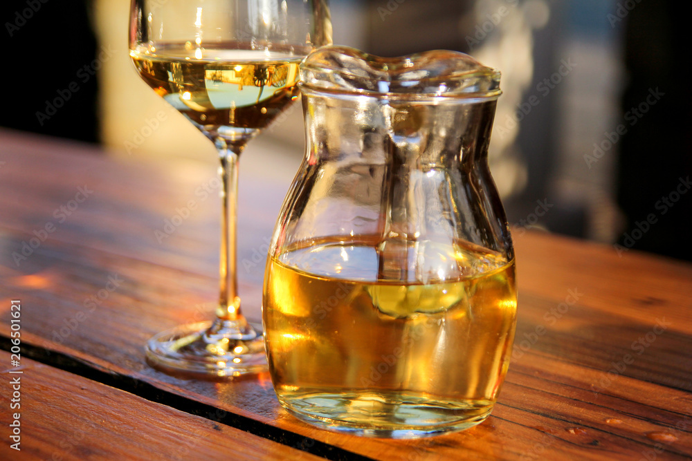 Bottle of white wine and glass on wooden table top. Glass of chilled white wine on table near the beach, in a restaurant tavern.