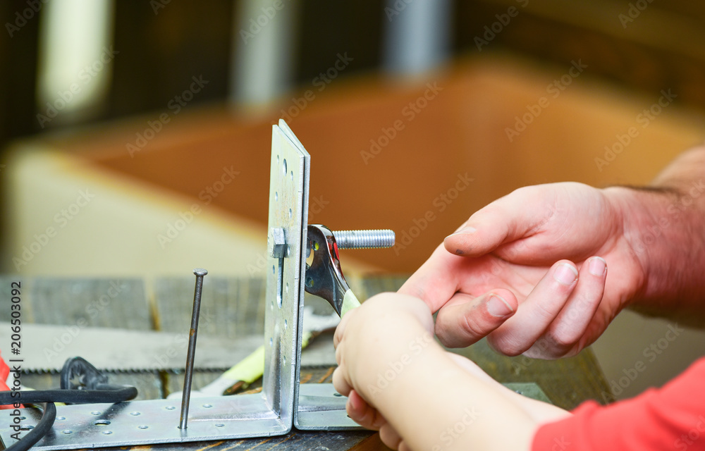 Father and son repairing together, close up. Repair and assistance concept. Childs hand helps adult to twist hex bolt. Male and childrens hands connecting metal plates, parts with hex bolt. Father and son repairing together, close up. Repair and assistance concept. Childs hand helps adult to twist hex bolt. Male and childrens hands connecting metal plates, parts with hex bolt.