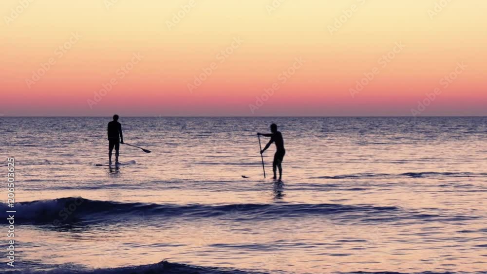 Two surfers on a beautiful pink background of the setting sun. Seascape. Two surfers on a beautiful pink background of the setting sun. Seascape.