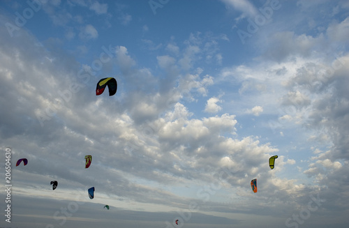 group of wings or kites used to practice kitesurfing, extreme sport, in air on a day of strong wind, blue sky at sunset, light and clouds, spring, ligurian riviera, italy, mediterranean sea