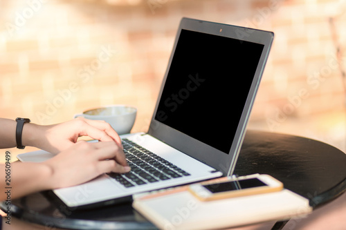 Close-up of Business female working with Mockup image of laptop with blank black screen coffee and smart phone on office outdoor.