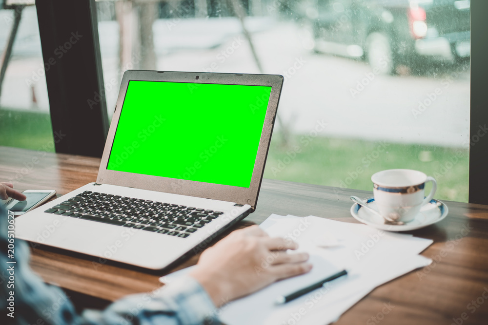 Close-up of businessman working with mockup image of laptop with blank green screen and smartphone in coffee shop like the background. Close-up of businessman working with mockup image of laptop with blank green screen and smartphone in coffee shop like the background.