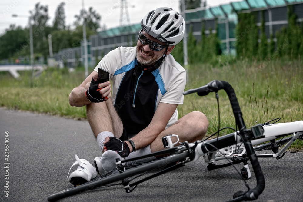 Fototapeta premium Injured biker holding his smartphone calling rescue team