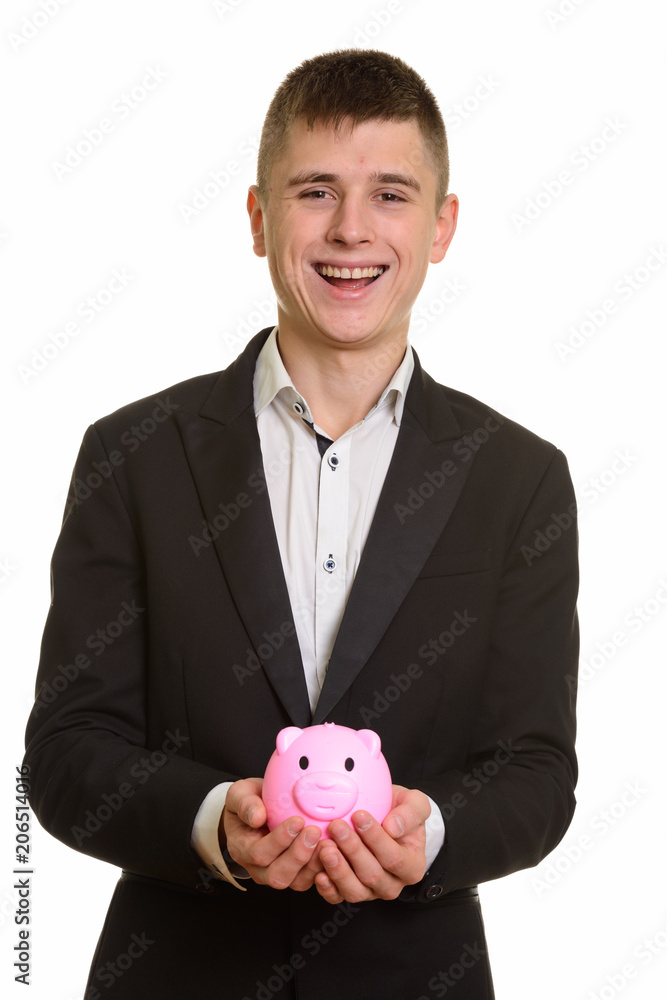 Studio shot of young happy businessman smiling and holding piggy Studio shot of young happy businessman smiling and holding piggy