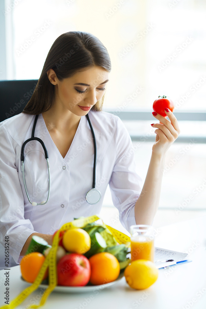 Health. Health Dietitian Sits At A Table With Fruits And Vegetables. The Doctor Draws up a Nutrition Plan. The Doctor Smiles at Vibrating Happy and Holds in the Tomatoes Hands.High Resolution Health. Health Dietitian Sits At A Table With Fruits And Vegetables. The Doctor Draws up a Nutrition Plan. The Doctor Smiles at Vibrating Happy and Holds in the Tomatoes Hands.High Resolution