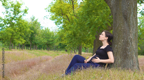 A young, beautiful, pregnant girl sits under a tree in a black T-shirt © malinad