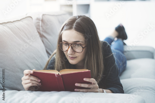 Young girl reading book while lying on couch at home