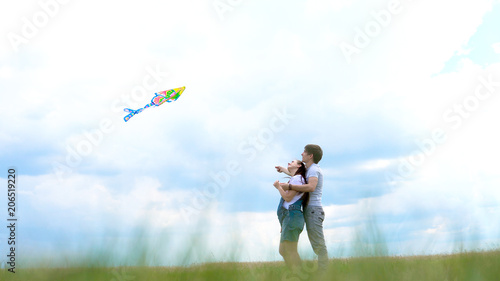 Young family, couple running a kite against a blue sky and clouds