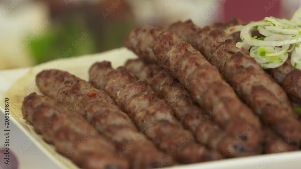 Dinner table served with lula kebabs and fresh vegetables. People enjoy Armenian style kebab at restaurant. Dinner table served with lula kebabs and fresh vegetables. People enjoy Armenian style kebab at restaurant.