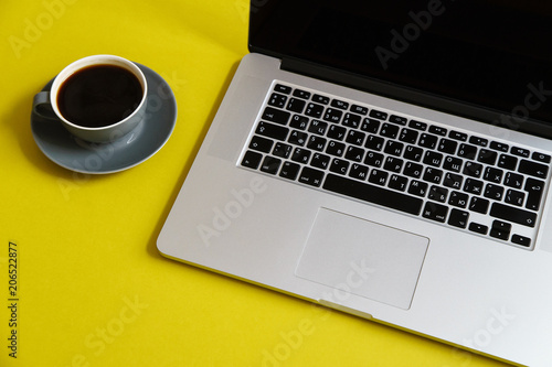 Flat lay with laptop and coffee cup on bright olive yellow background with copy space