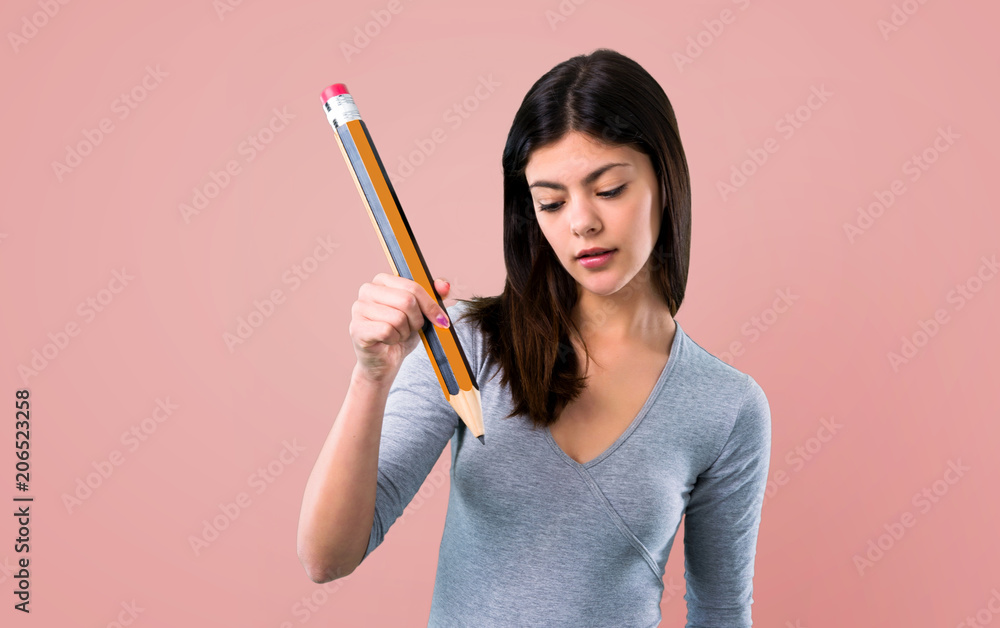 Teenager girl holding a big pencil on pink background Teenager girl holding a big pencil on pink background