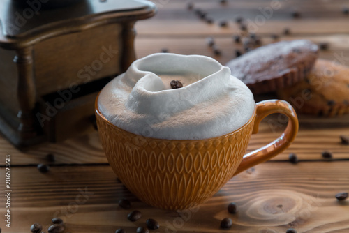 Cup of coffee with foam in the form of a heart with cookies and coffee beans with coffee grinder on a wooden table