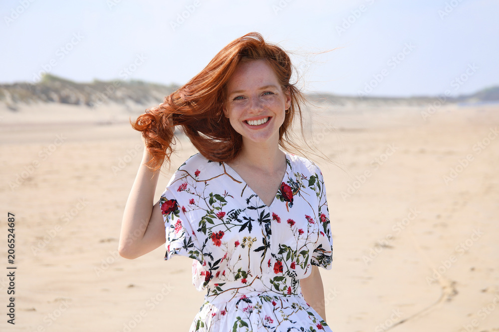 Hübsche rothaarige Frau steht an einem Strand und lacht Hübsche rothaarige Frau steht an einem Strand und lacht