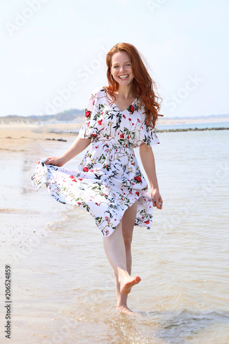 Hübsche rothaarige Frau in einem Kleid läuft durch seichtes wasser am Meer und lacht