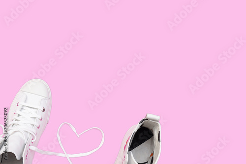 Top view of white sneaker with heart sign made of shoelaces on pastel pink background. Love Valentine's day concept.Copy space empty blank for text.Flat lay design.