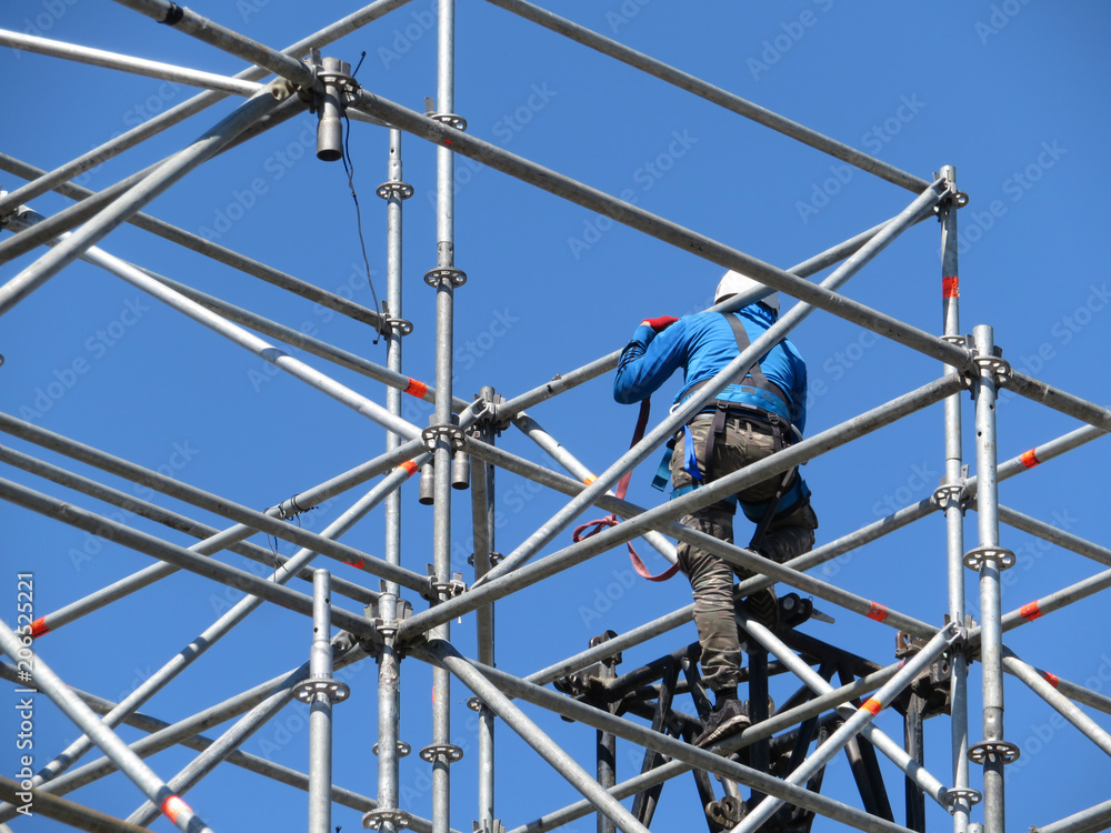Construction worker working on scaffolding. Steeplejack on the background of clear blue sky