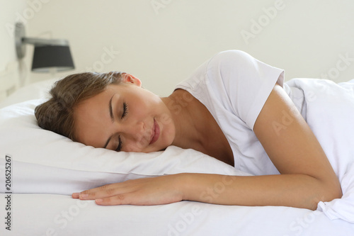 Hübsche junge Frau liegt in einem Bett und lächelt mit geschlossenen Augen