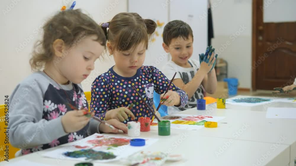 Children's developing a game room. Emotions of young children during entertaining classes. children paint with finger paints on white sheets of paper. children stretch their hands in the paint smeared Children's developing a game room. Emotions of young children during entertaining classes. children paint with finger paints on white sheets of paper. children stretch their hands in the paint smeared
