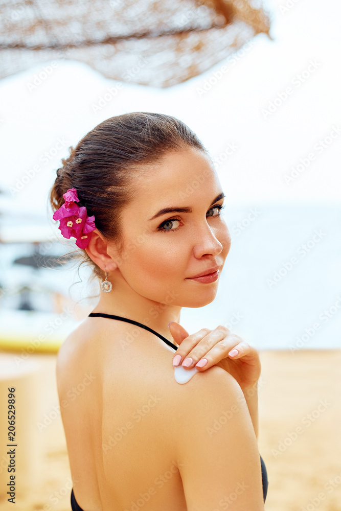 Sunscreen woman. Girl putting sun block on beach holding white sun tan  lotion bottle. Beautiful young woman in bikini smear protective cream on  the skin on the beach under the sun. Stock