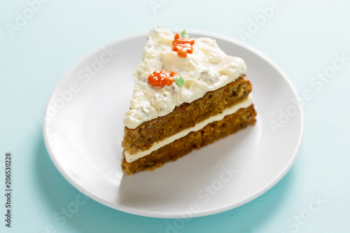 Slice of carrot cake with frosting and carrot decoration. 
