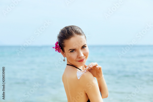 Woman applying sunscreen creme on tanned shoulder. Skincare. Body Sun protection sun cream. Bikini woman smear moisturizing lotion on back.
