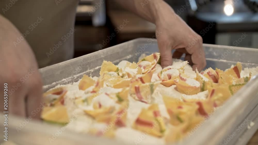 Hands of an unrecognizable man putting tortellini in a box and sprinkling them with flour. Concept of traditional cuisine and agriculture. Left to right pan real time medium shot Hands of an unrecognizable man putting tortellini in a box and sprinkling them with flour. Concept of traditional cuisine and agriculture. Left to right pan real time medium shot