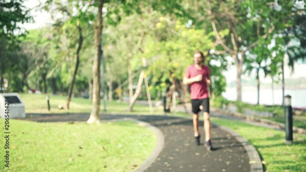 Young LGBT running and looking at his smart watch in park. White male in red tshirt stretching running in a public park into focus shot and look at his smart watch. Sport tech concept. Young LGBT running and looking at his smart watch in park. White male in red tshirt stretching running in a public park into focus shot and look at his smart watch. Sport tech concept.