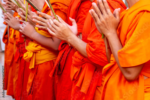 The group of monks in the orange robe are greeting with flower candle and stick incense in hands at the temple.