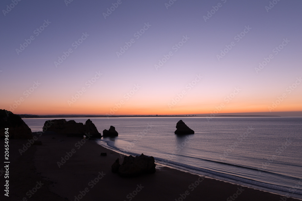 Sunrise over the ocean in Lagos, Portugal. Empty sandy beach with rock formations at sunrise.