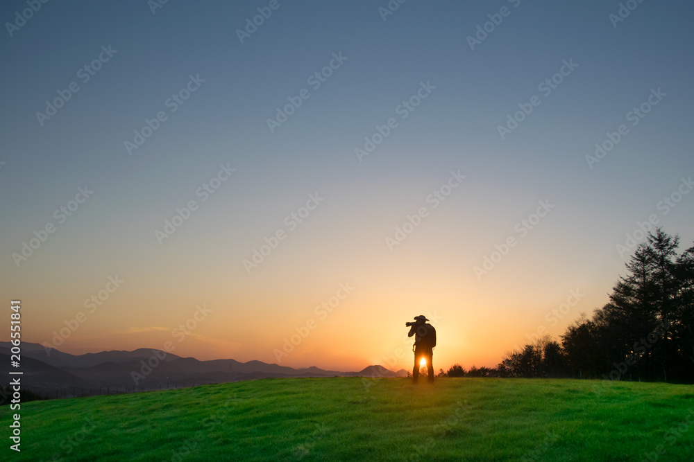 A man photographer taking pictures of sunset on the hill