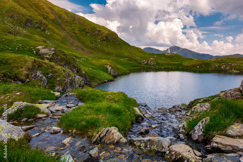 rapid streams flow to lake Capra in mountains. Fagaras mountain ridge under the gorgeous cloudscape in the distance. Beautiful summer landscape of Romania