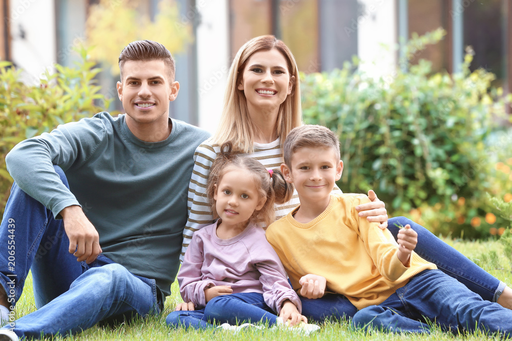 Fototapeta premium Happy family sitting on green grass in courtyard near their house