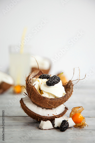 creative presentation of ice cream in coconut shell, decorated with mulberry and physalis berries photo