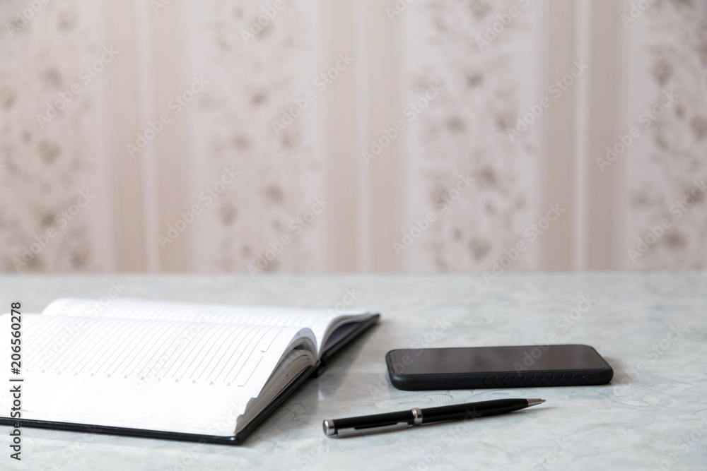 A blank notebook, pen and a smartphone on a grey table A blank notebook, pen and a smartphone on a grey table